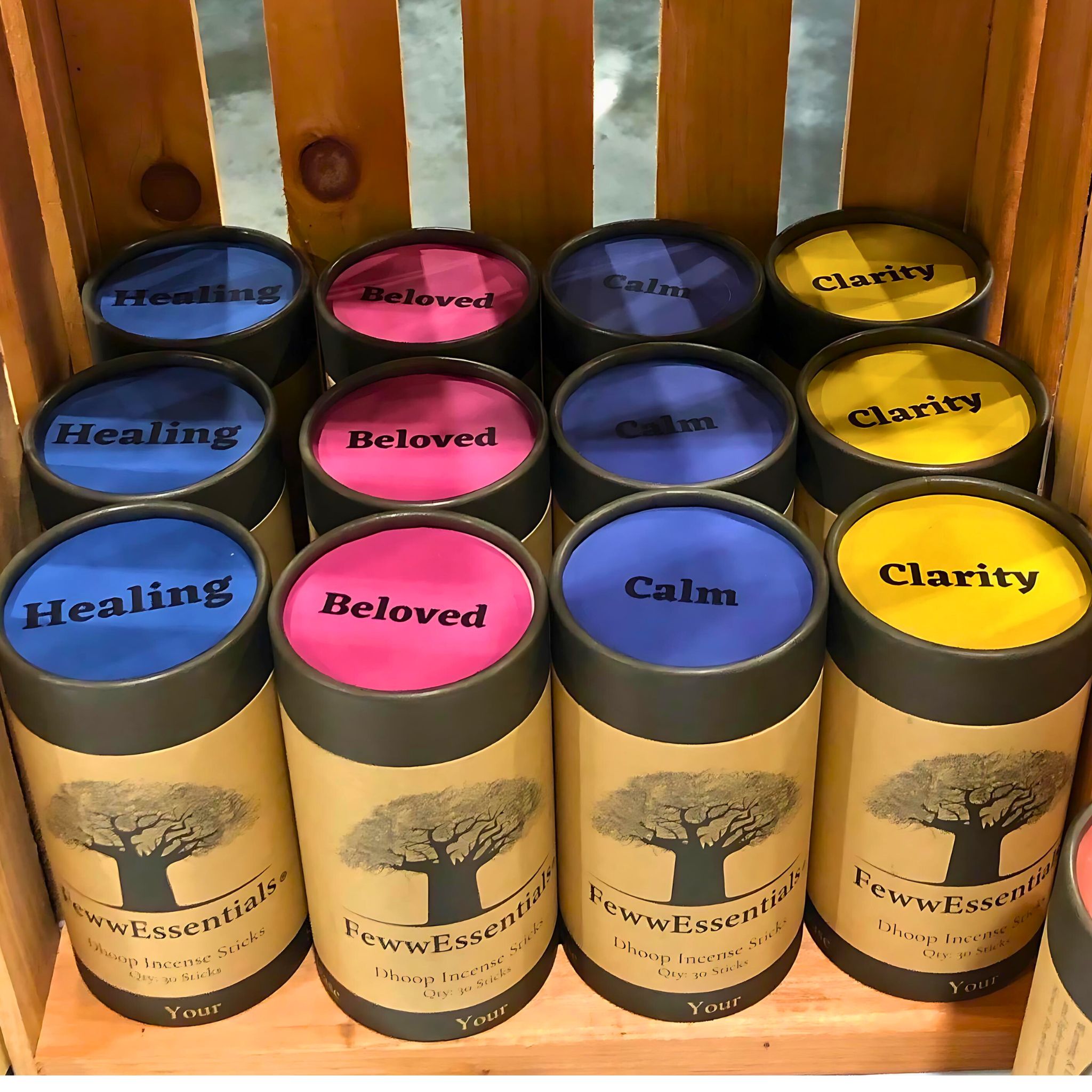 "A neat display of FewwEssentials Dhoop Incense Sticks in a wooden shelf, showing various colors and labels including Healing, Beloved, Calm, and Clarity."