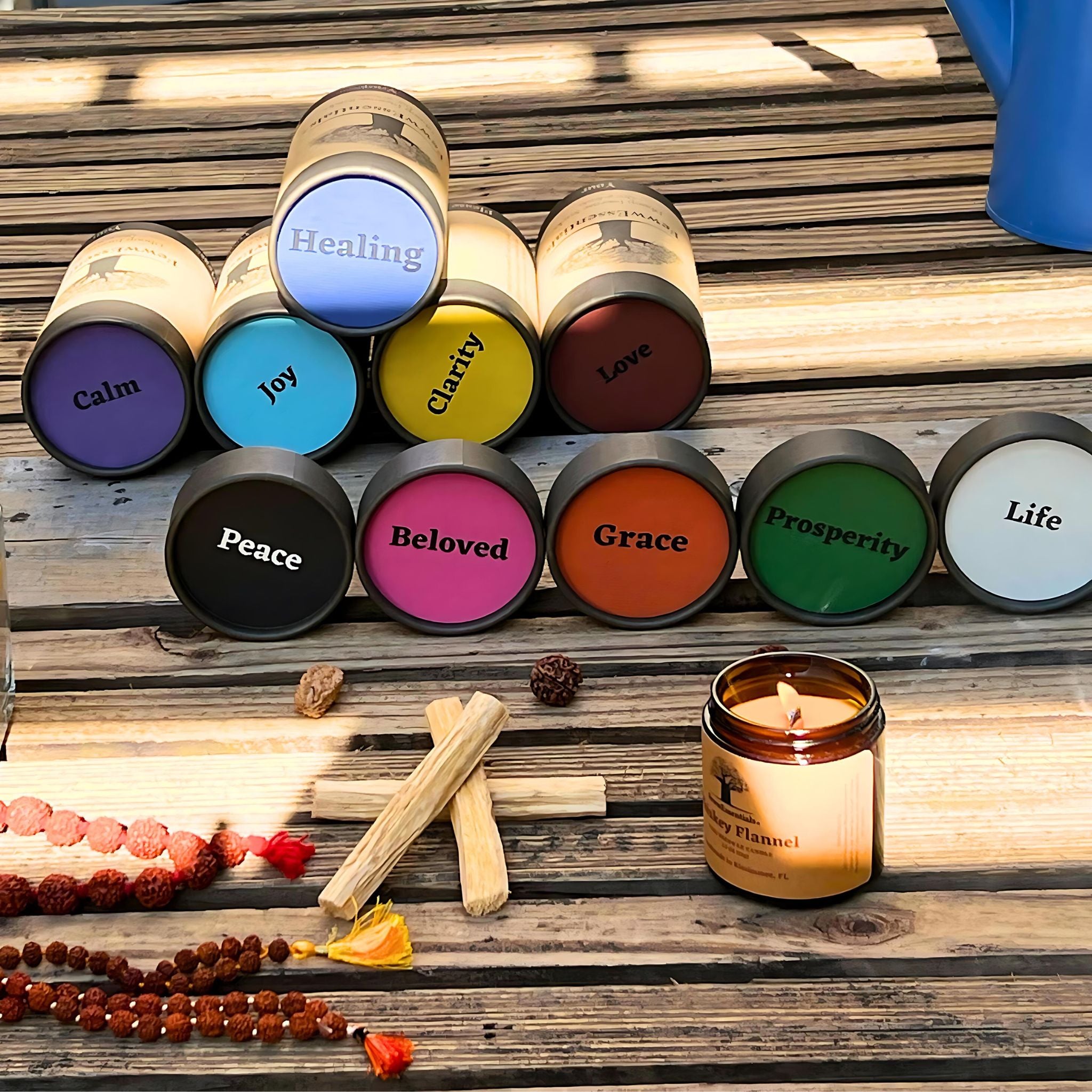 Stacked FewwEssentials Dhoop Incense Sticks on a wooden surface, showcasing labels such as Healing, Joy, Clarity, Love, Peace, Beloved, Grace, Prosperity, and Life, with a burning candle and rudraksha beads.