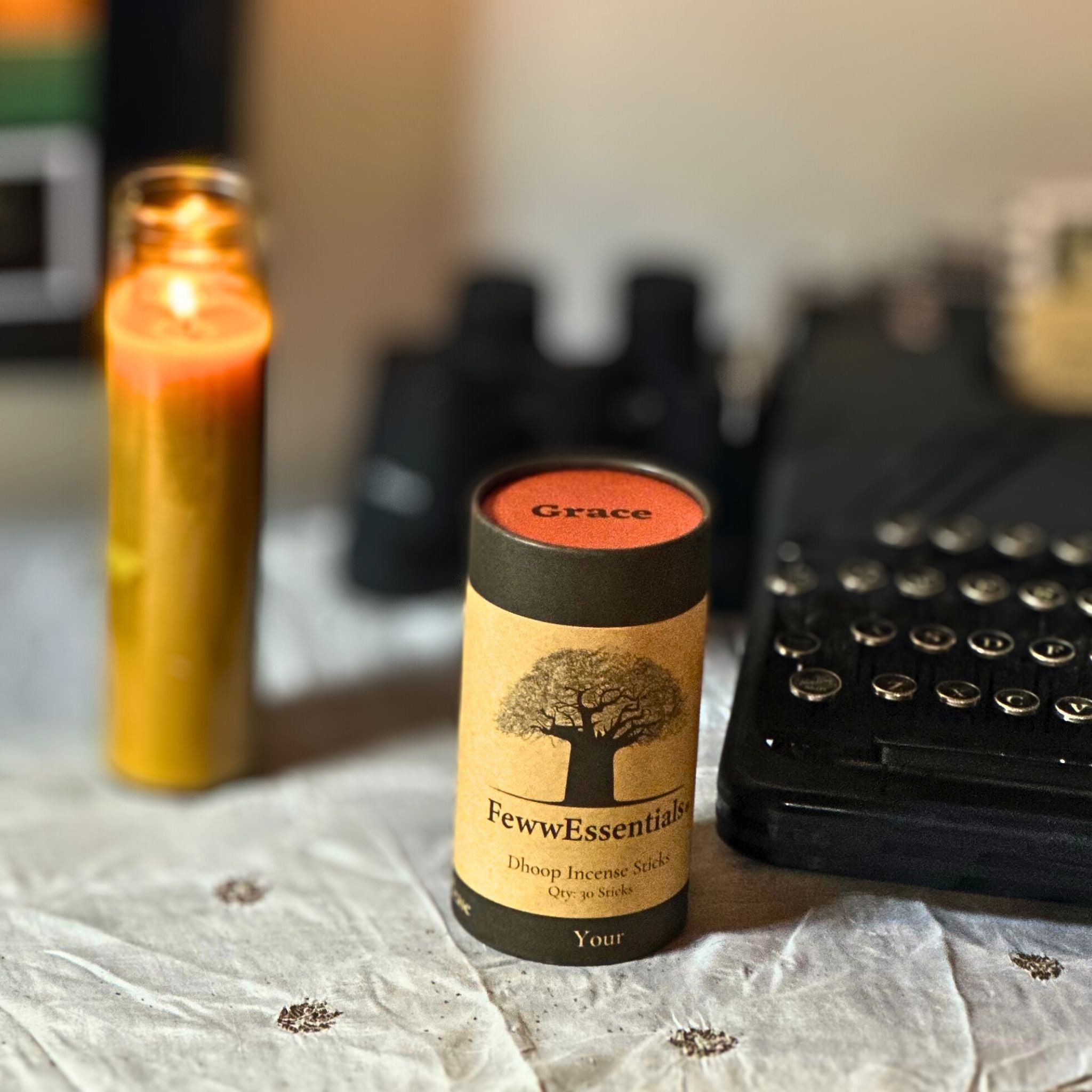 "A cozy desk scene with FewwEssentials Dhoop Incense Sticks labeled Grace, a burning candle, and a vintage typewriter."