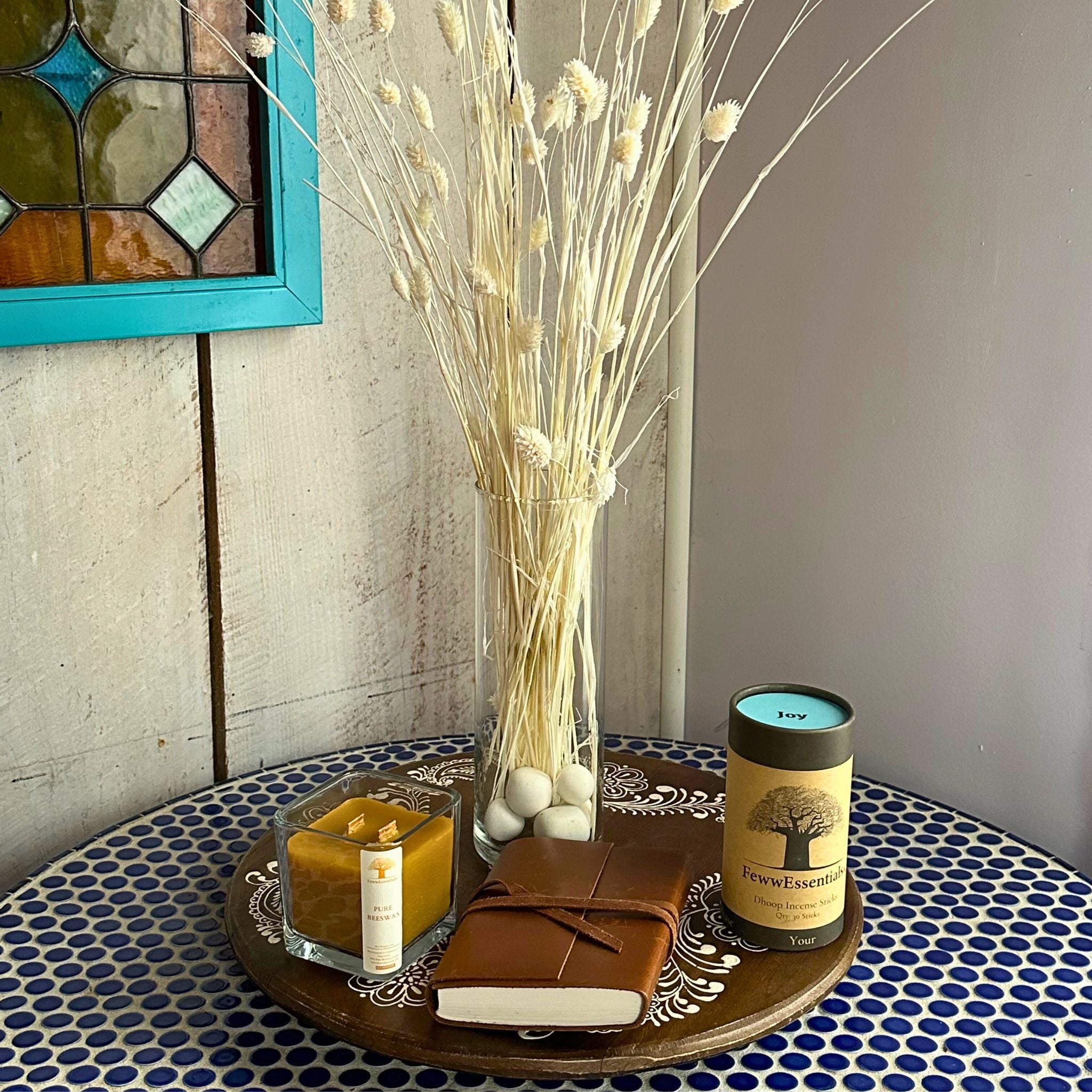 "A table with FewwEssentials Dhoop Incense Sticks labeled Joy, a candle, and a leather journal with dried floral decor in the background."